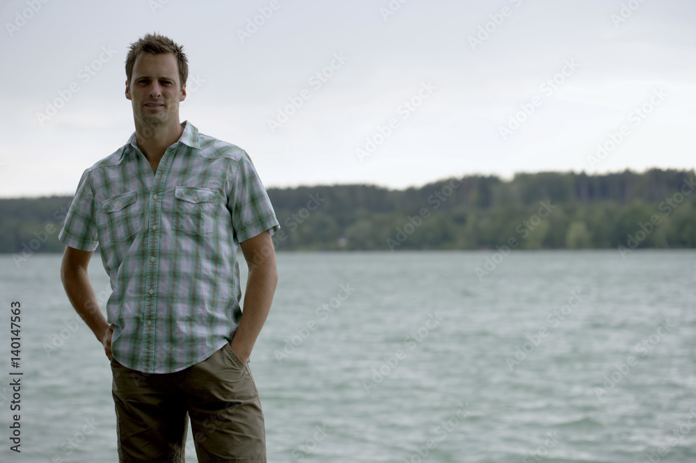 Mid adult man is standing in front of a lake, selective focus