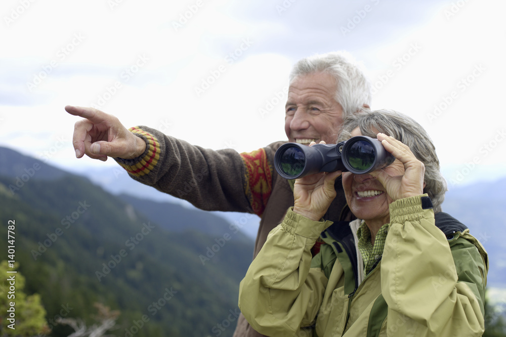 Senior adult couple with binoculars in the mountains, close-up, selective focus Senior adult couple with binoculars in the mountains, close-up, selective focus
