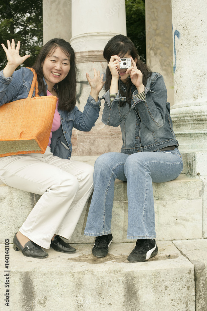 Two Asian women sitting on the stairs of a monument, one of them with a camera in her hand