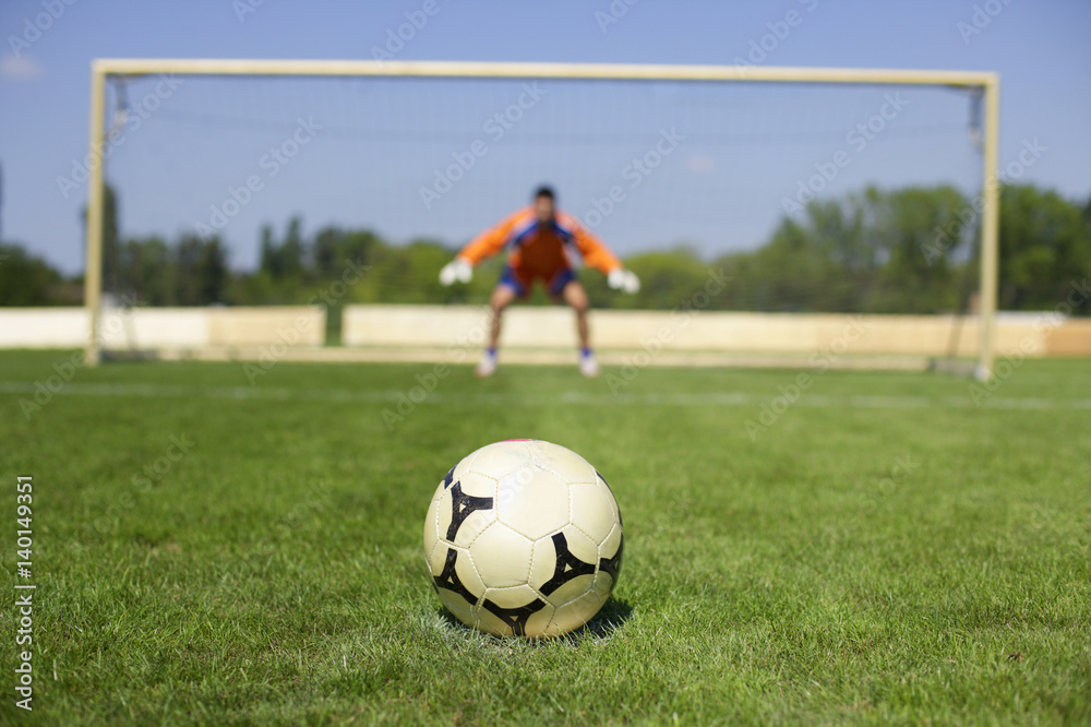 Obraz premium Ball lying on grass, goalkeeper in background