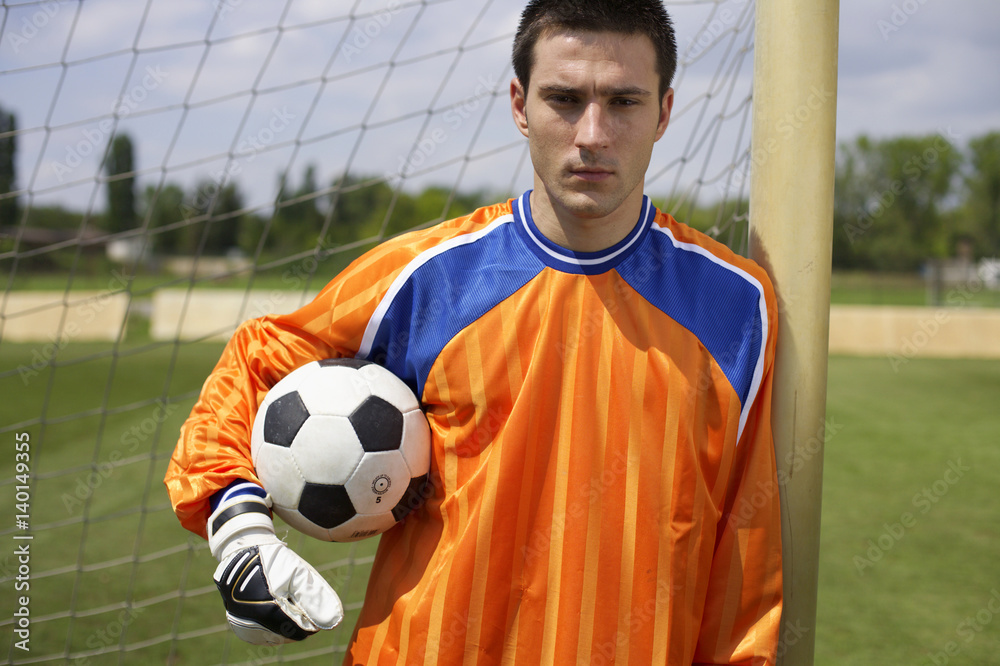 Fototapeta premium Goalkeeper holding ball leaning against goal, portrait