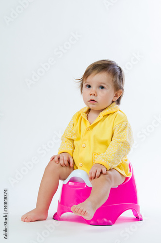 Little smiling girl sitting on a pot. Isolated on white background.