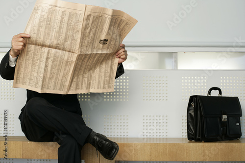 Businessman sitting on a bench reading a newspaper