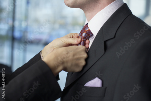 Businesswoman binding the tie of her colleague, close-up