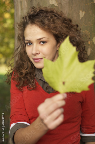Teenage girl with curly hair in front of a log is holding a leaf in her hand  selective focus  close-up