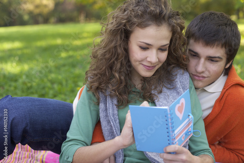 Teenage girl writing a postcard in front of a teenage boy, close-up, selective focus