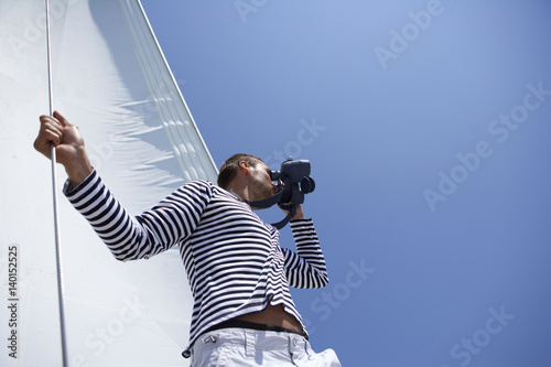 Man standing in front of a sail, looking through a spyglass, low angle view
