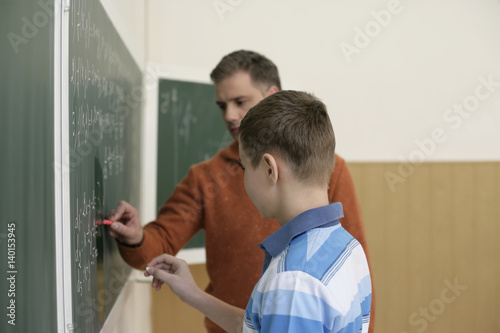 Teacher and teenage boy writing on blackboard