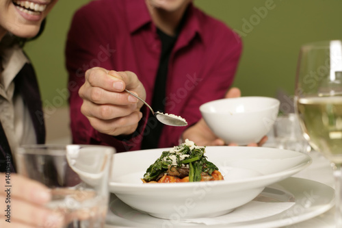 Man strewing parmesan over woman's tagliatelle