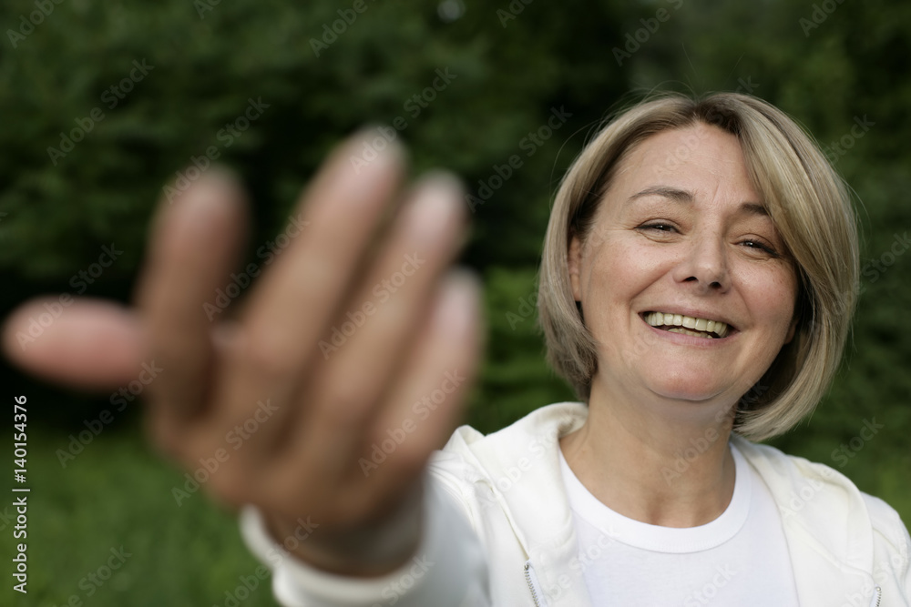 Mature woman smiling at camera, stretching her arm Mature woman smiling at camera, stretching her arm