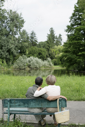 Mature couple sitting on a bench, looking at a small lake