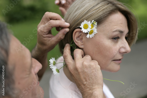 Mature man putting flowers behind woman's ear
