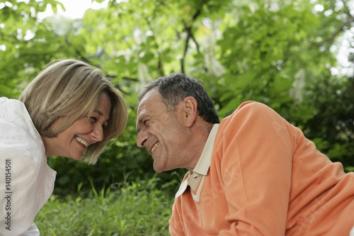 Laughing mature couple lying on grass and looking into each other's eyes