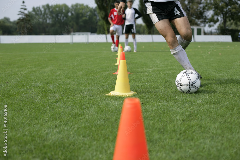 Fototapeta premium Soccer player running with football slalom around pylons