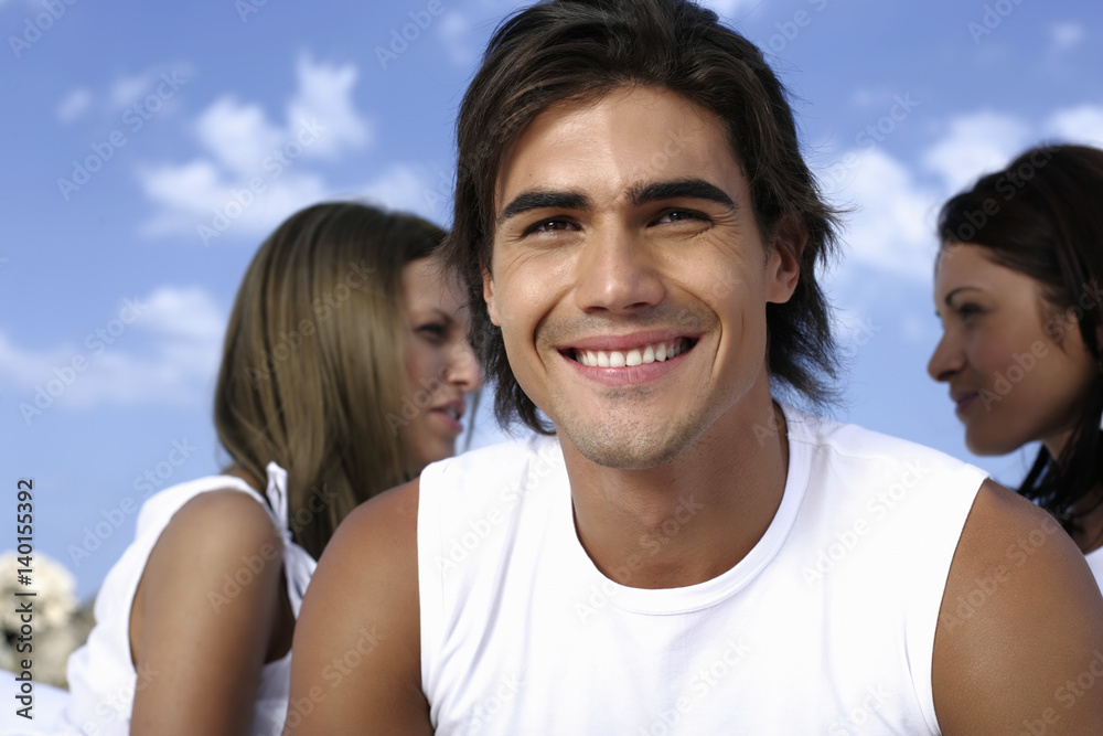 Man laughing at camera, two women sitting in background Man laughing at camera, two women sitting in background