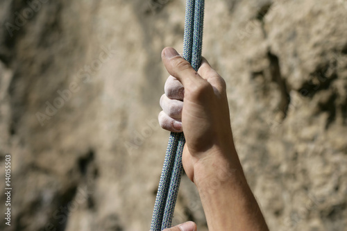 Dirty male hand touching a rope in front of a rocky wall, close-up, selective focus