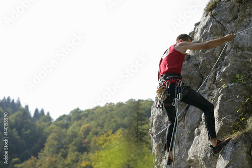 Young man climbing up a rocky wall, selective focus