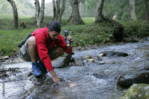 Young man with black hair is illuminating a spot of a rivulet with a flashlight