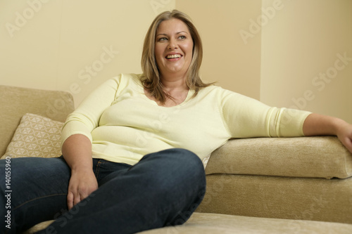 Overweight young woman with blond hair is sitting on a settee