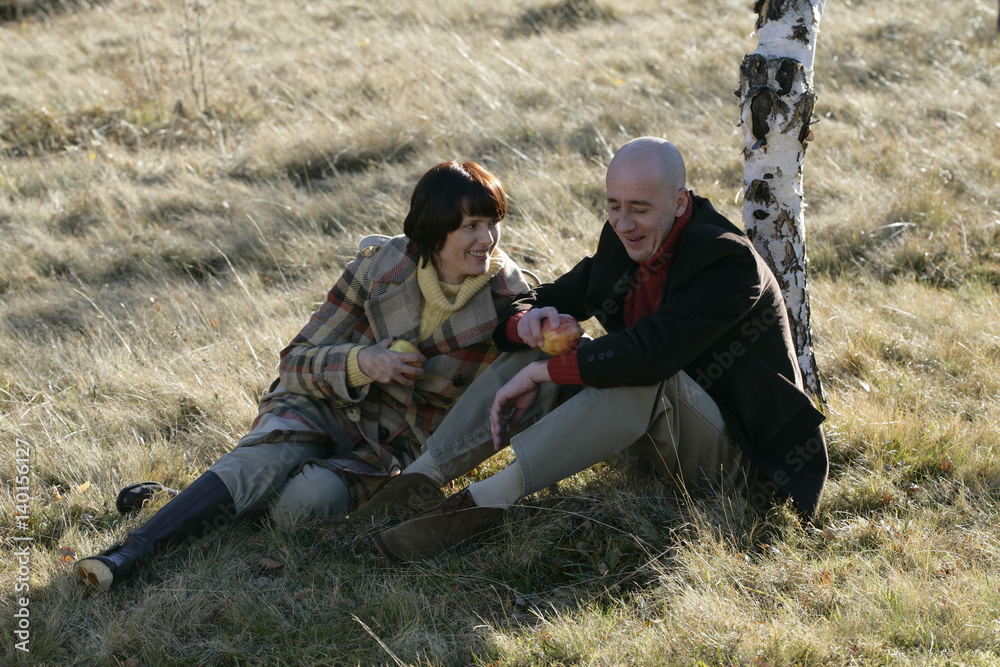 Mature couple sitting on grass and holding fruits in their hands