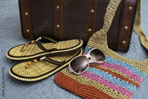Tropical sandals, purse, sunglasses and suitcase lying on bed, ready for travel
