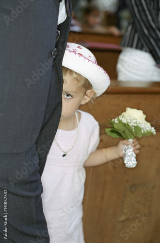 Little Girl in a white Dress with a Bunch of Flowers in her Hand hiding behind a Grown-Up - Bashfulness - Church - Celebration - Baptism - Christianity photo