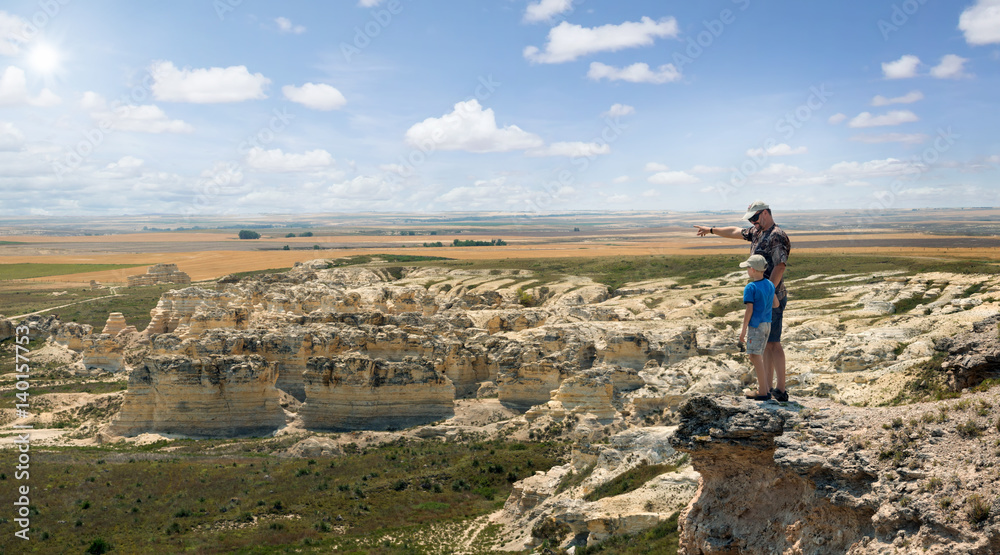 Father and son stand on the rock and look at the horizon line. Castle Rock Badlands. Western Kansas, US
