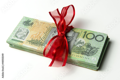 Bundle of Australian $100 notes, tied up with red ribbon, like a gift, nice shadow. copyspace.