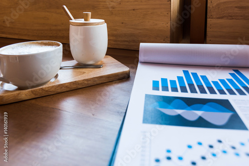 Coffee cup  on a table with laptob and graph finance diagram in coffee shop