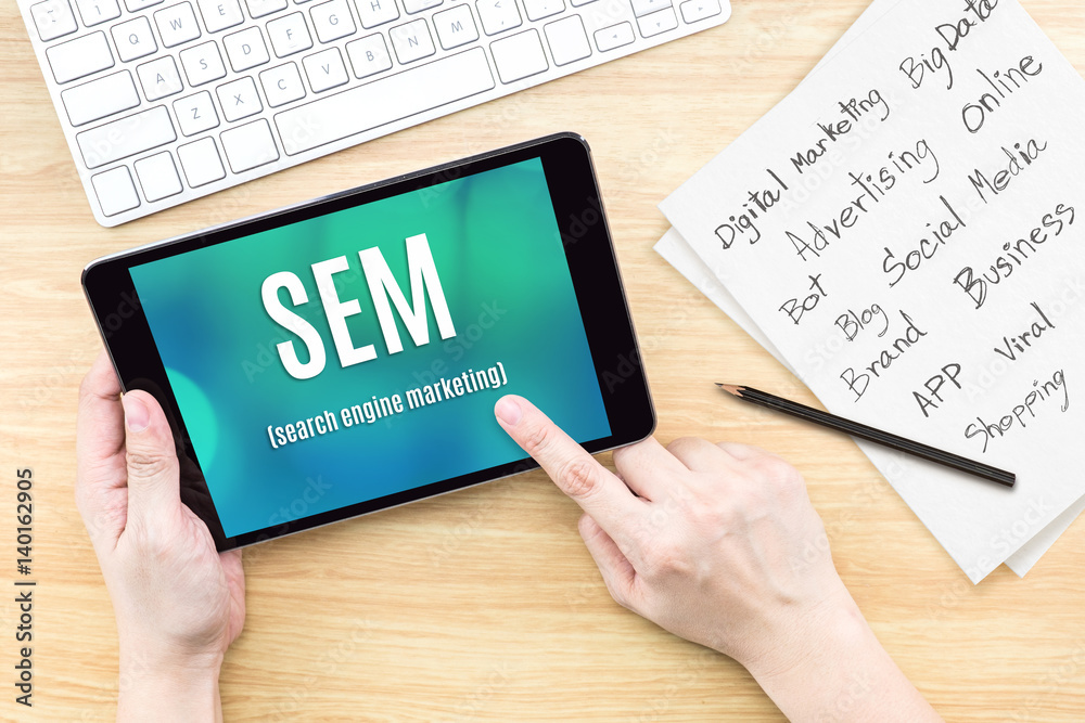 Hand using tablet with SEM (Search engine marketing ) word on screen with list of digital marketing features on paper on work table,Online business concept Hand using tablet with SEM (Search engine marketing ) word on screen with list of digital marketing features on paper on work table,Online business concept