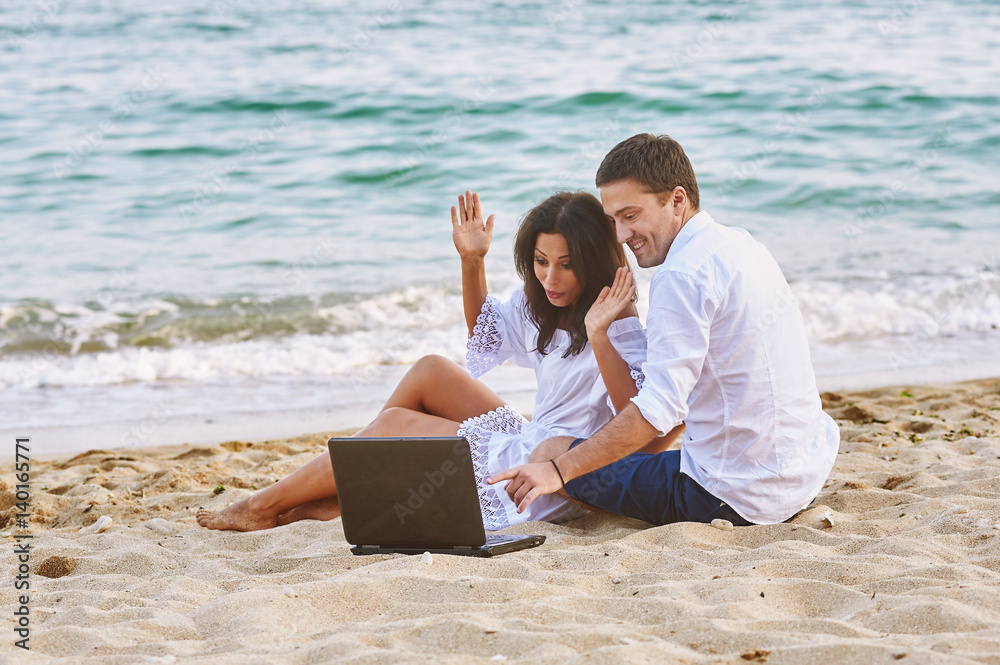 young romantic couple on the beach with a laptop