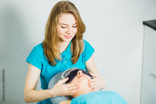 Portrait of beautician in turquoise t-shirt doing facial massage on wyite background photo