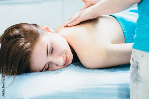 Close up young woman lying vestured turquoise towel while massage therapist massaging her shoulders. Beauty, health life and cosmetology concept.