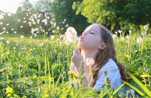 Teen blowing seeds from a dandelion flower in a spring park