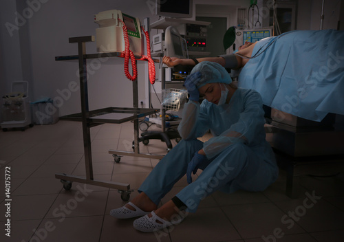 Sad doctor sitting on floor after failed operation in clinic