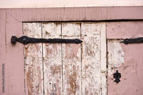 Old wooden locked door with peeling dusty pink paint. Closeup.