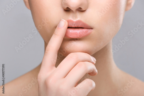 Woman with cold sore touching lips on light background