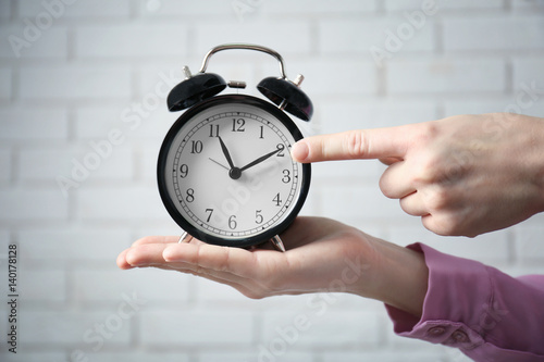 Female hands holding alarm clock on white brick wall background photo
