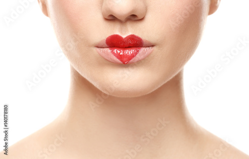Beautiful young woman with heart painted on lips against white background, closeup