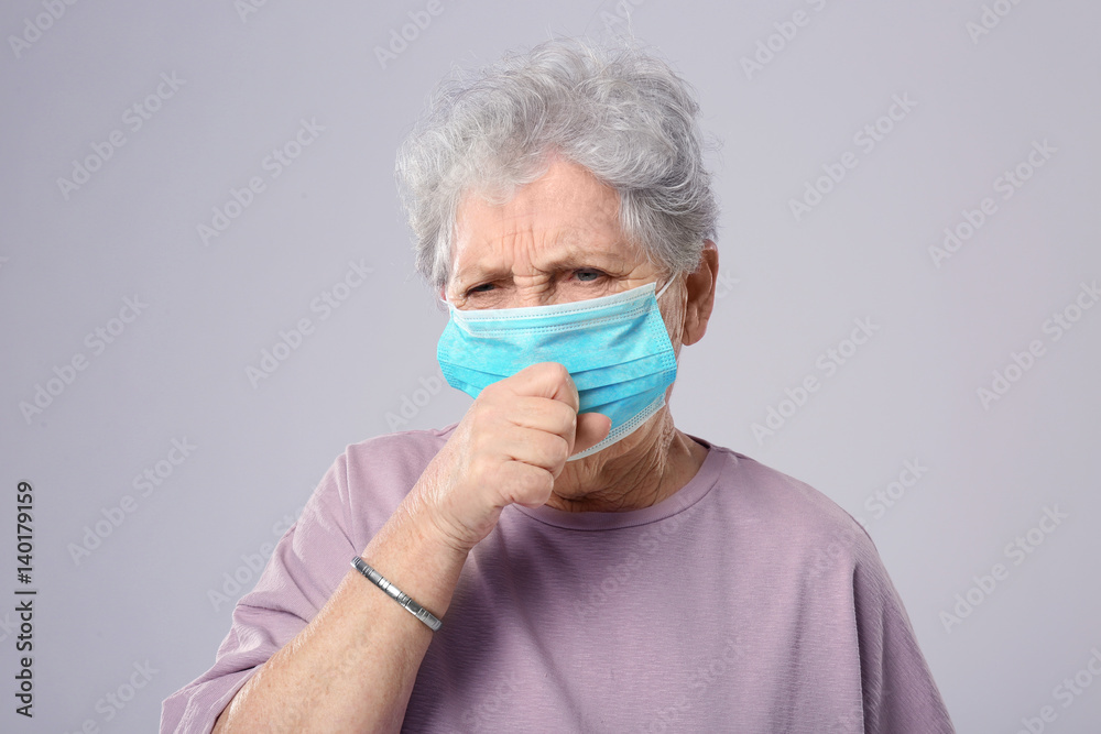 Portrait of coughing elderly woman wearing protective mask on grey background Portrait of coughing elderly woman wearing protective mask on grey background