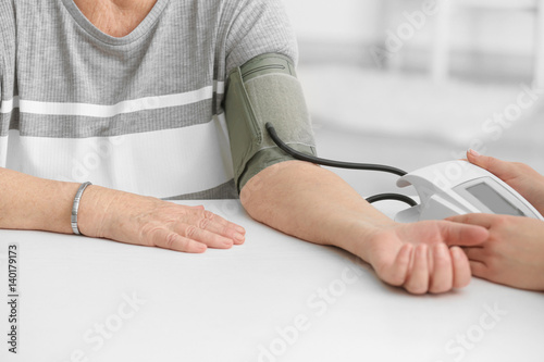Doctor measuring pressure of elderly woman with digital sphygmomanometer while sitting at table