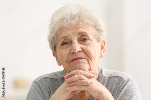 Portrait of elderly woman propping face with hands in light room