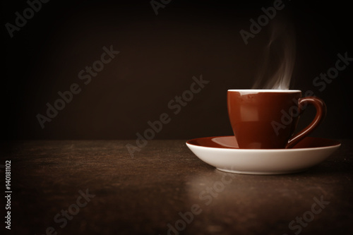 Steaming cup of coffee on table and black background