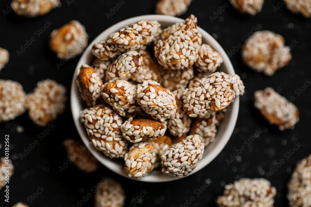 Closeup shot of peanuts covered with sesame in white bowl on a black wooden table, top view, shallow depth of field