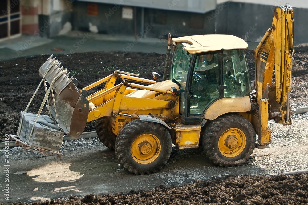 Heavy orange wheeled loader transporting pallet with concrete blocks attached on the front bucket of the machine. Worksite outdoors. Construction and renovation concept. 