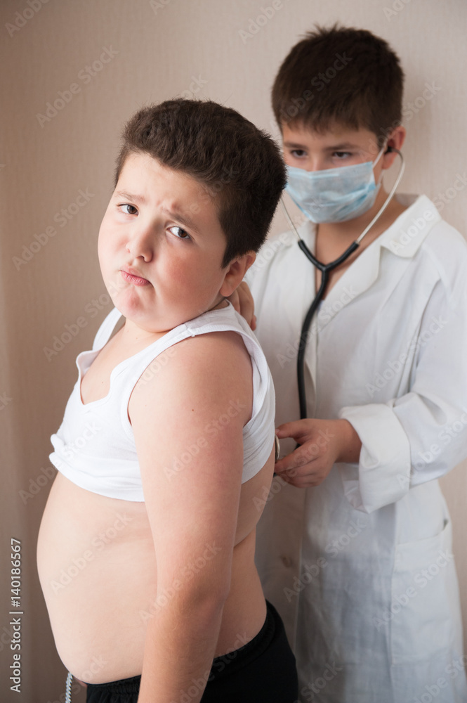 boy in costume of doctor checks heartbeat of fat boy with stethoscope