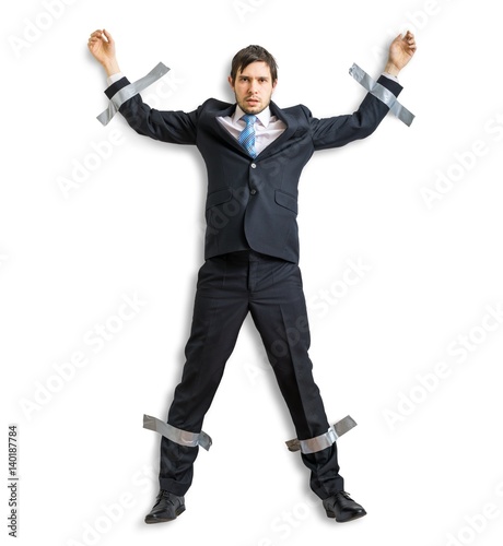 Businessman in suit is taped to the wall with adhesive tape. Isolated on white background.