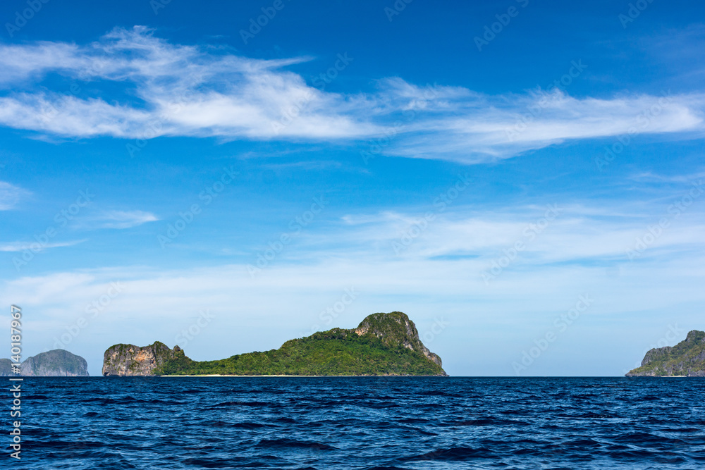 Distant view across a calm blue sea of Helicopter Island, El Nido, Philippines.
