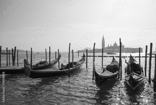 Gondolas in Venice, Italy tied to the pillars with San Giorgio church in the background, black and white © Neeqolah
