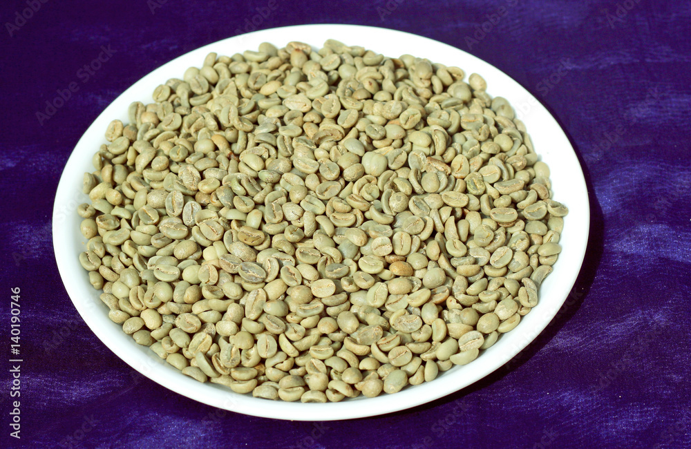 Green coffee or un-roasted coffee beans put into white plate on blue background.